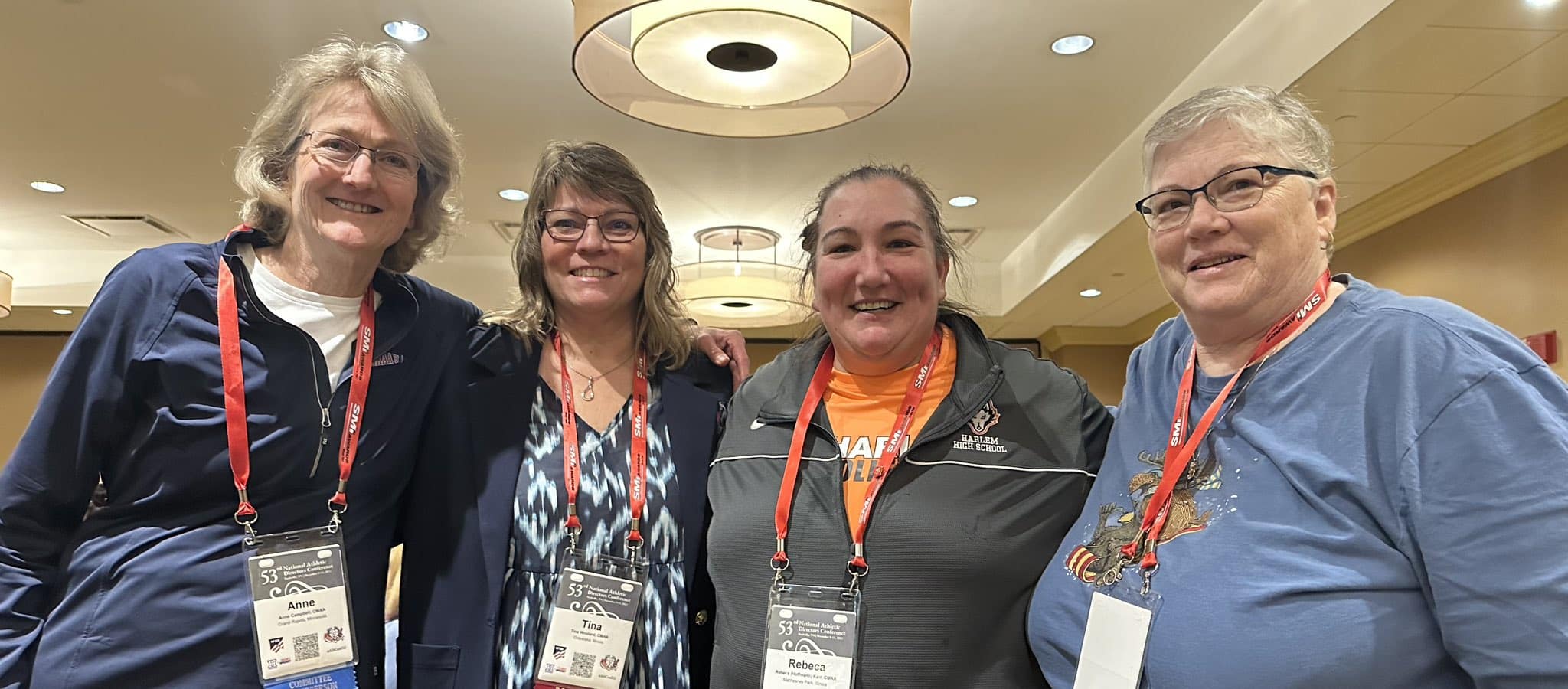 Four women wearing conference credentials standing together and smiling at a Global Community gathering.