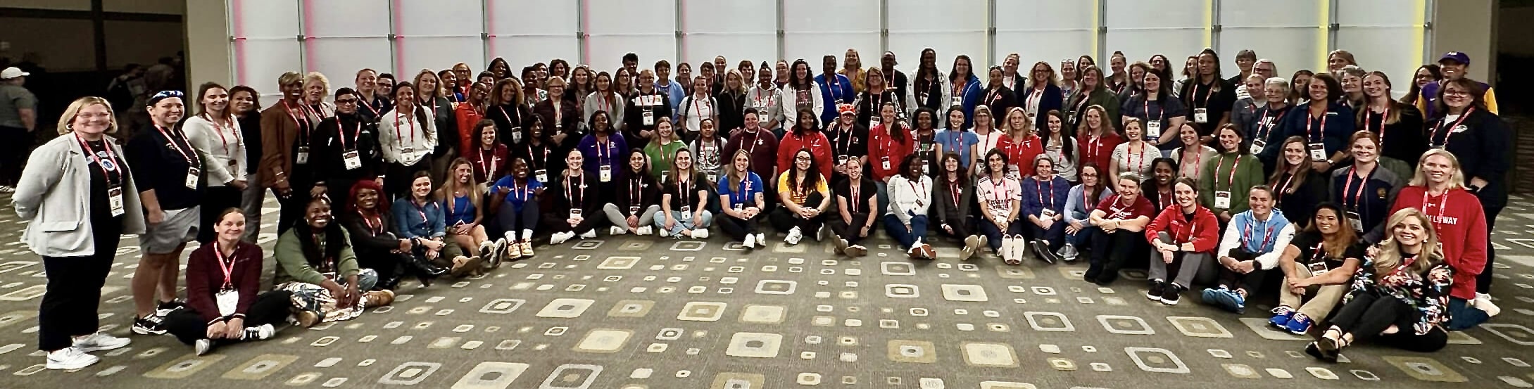 A large group of women gathered together at a conference, wearing event credentials.