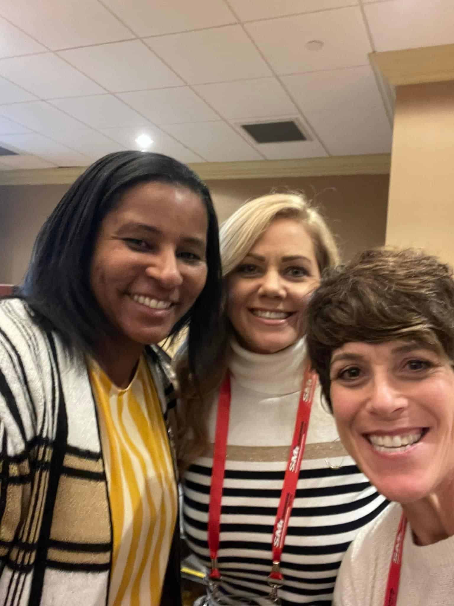 Three women standing close together and smiling at a Global Community of Women in High School Sports gathering.